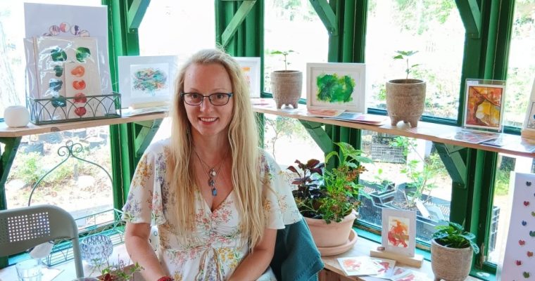 Dr. Daria Chrobok sitzt vor ihren Bildern in ihrer Ausstelung.